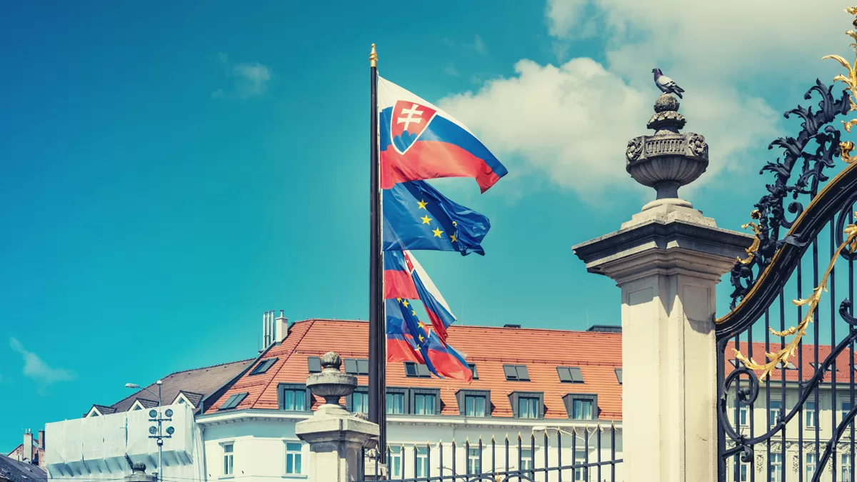 Slovenská a európska vlajka vejúce pred historickou budovou v Bratislave, symbolizujúce štátnosť a integráciu v čase krízy.