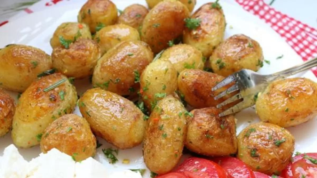 Pečené nové zemiaky s bylinkami a cesnakom, podávané s paradajkami a syrom na bielom tanieri.